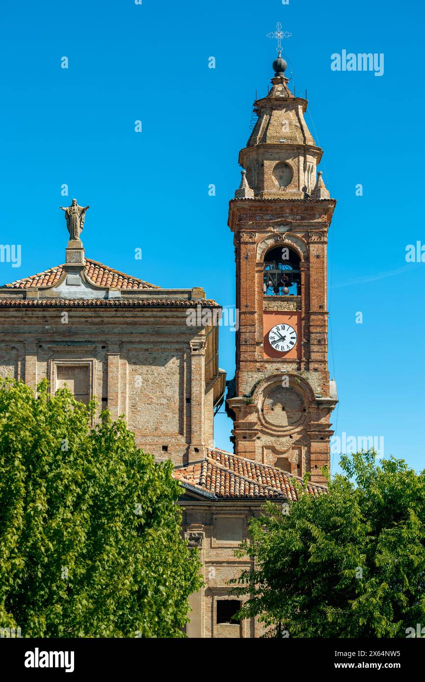 Vertikale Ansicht der alten Kirche und des Glockenturms mit Uhr unter blauem Himmel in der kleinen Stadt Diano d'Alba, Piemont, Italien. Stockfoto