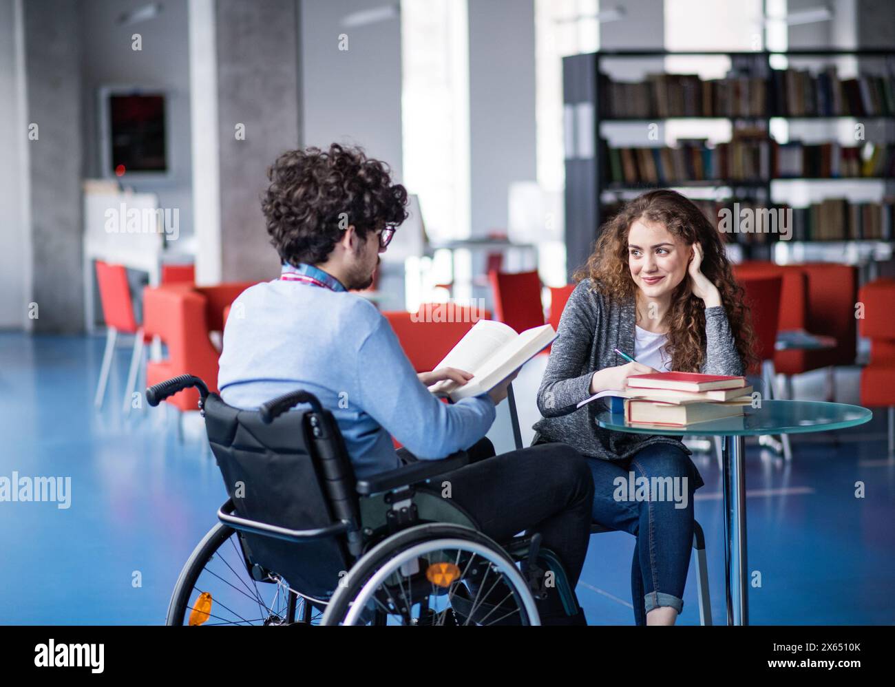 Gutaussehender Student im Rollstuhl, Studium in der Bibliothek mit Klassenkameraden, Vorbereitung auf die Abschlussprüfung, Präsentation. Studiengruppe. Teamfähigkeit. Stockfoto