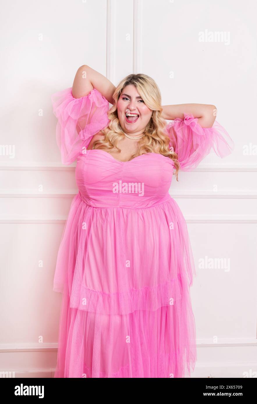 Strahlende Frau in Übergröße posiert im Studio mit Aufregung in einem stilvollen rosa Kleid Stockfoto
