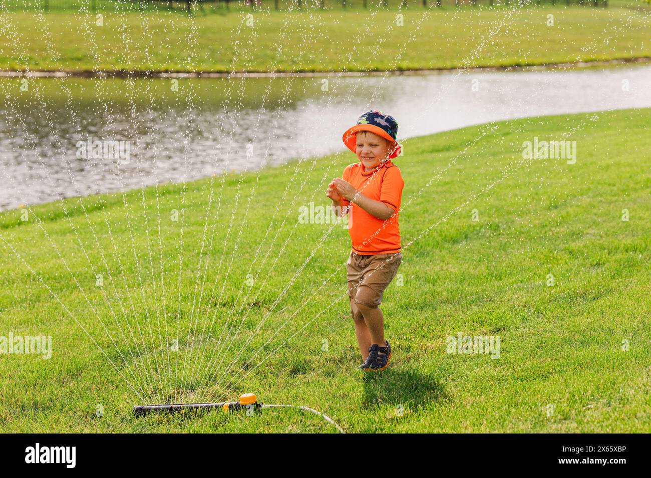 Fröhliches Kind, das an sonnigem Tag im Sprinkler spielt Stockfoto