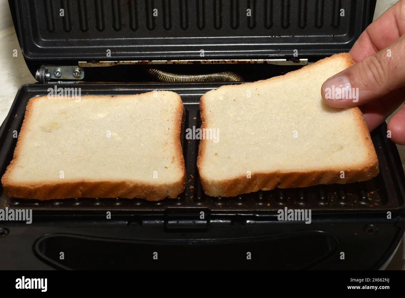 Auf dem Foto legt die Hand eines Mannes Toast auf die elektrische Grillplatte. Stockfoto