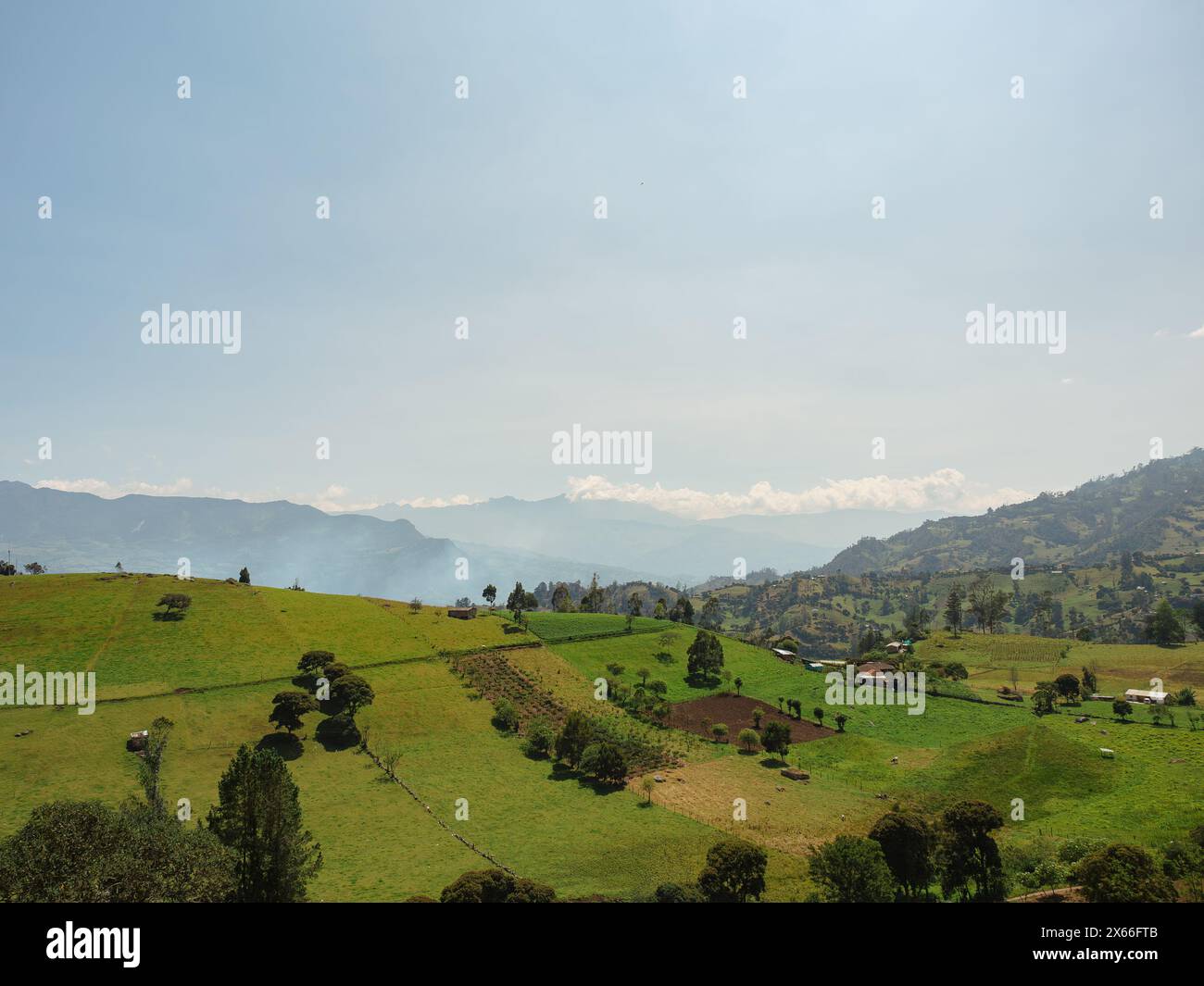 Hügellandschaft auf dem Land mit Feldern, Bäumen, grünen Wiesen und Bergen im Hintergrund Stockfoto
