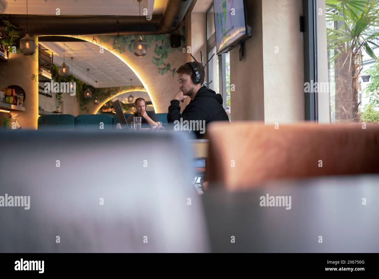 Belgrad, Serbien, 3. Mai 2024: Ein junger Mann, digitaler Nomad sitzt an einem Computer, Kopfhörer an, in einem Café in Zemun. Stockfoto