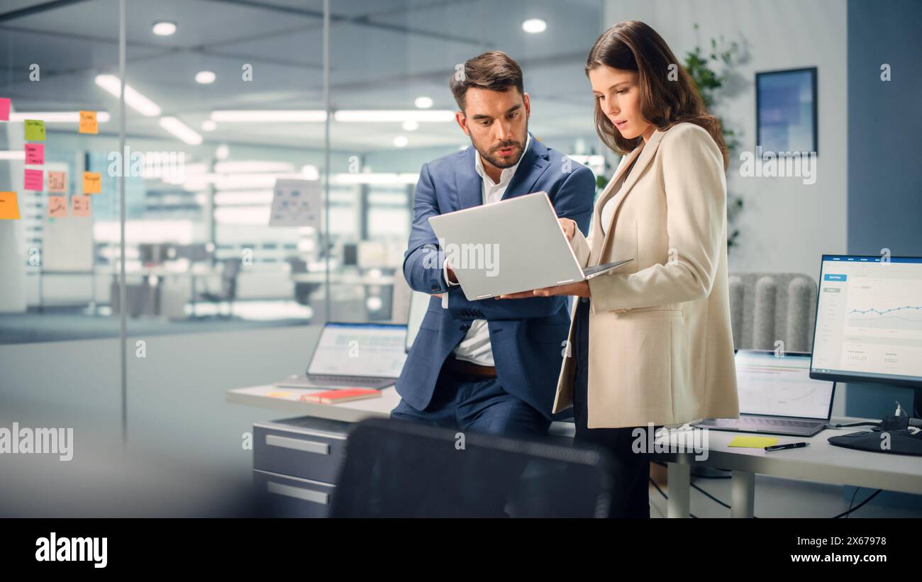 Junger Manager, der mit einem erfahrenen Kollegen spricht, während er im Büro einen Laptop verwendet. Kollegen diskutieren Geschäfts-, Finanz- und Marketingprojekte. Spezialisten arbeiten in diversen Teams. Stockfoto