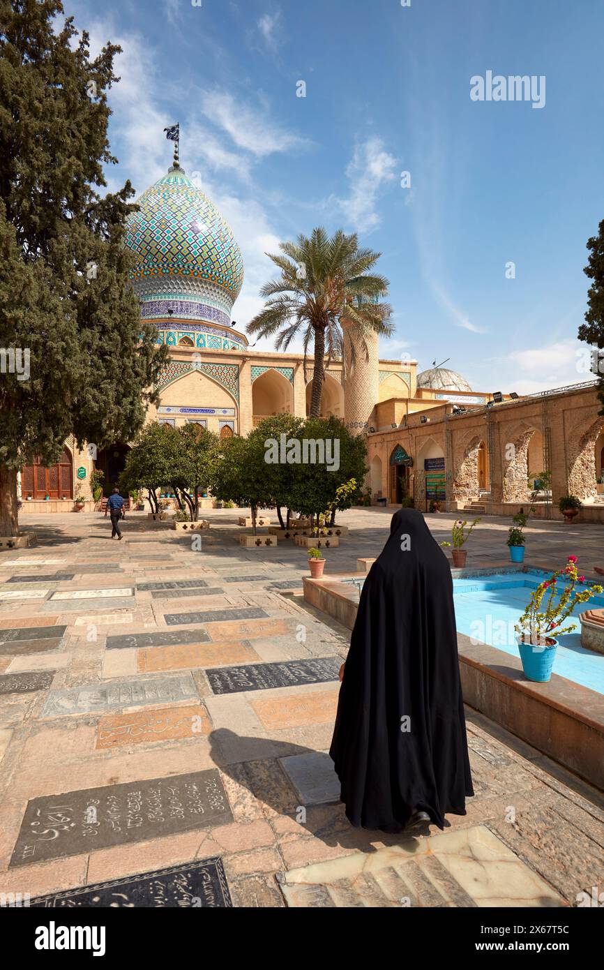 Iranische Frau mit schwarzem Chador geht im Innenhof des Heiligtums von Ali Ibn Hamzeh. Shiraz, Iran. Stockfoto