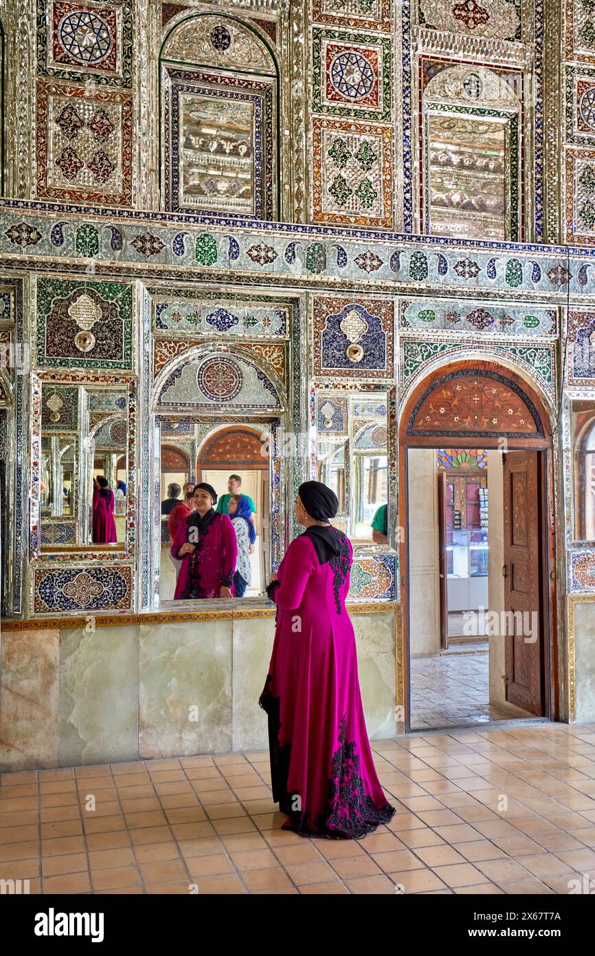 Die iranische Frau in einem schicken Kleid schaut in den Spiegel des Zinat Al-Molk Historical House, einer Residenz aus der Qajar-Zeit aus dem 19. Jahrhundert. Shiraz, Iran. Stockfoto