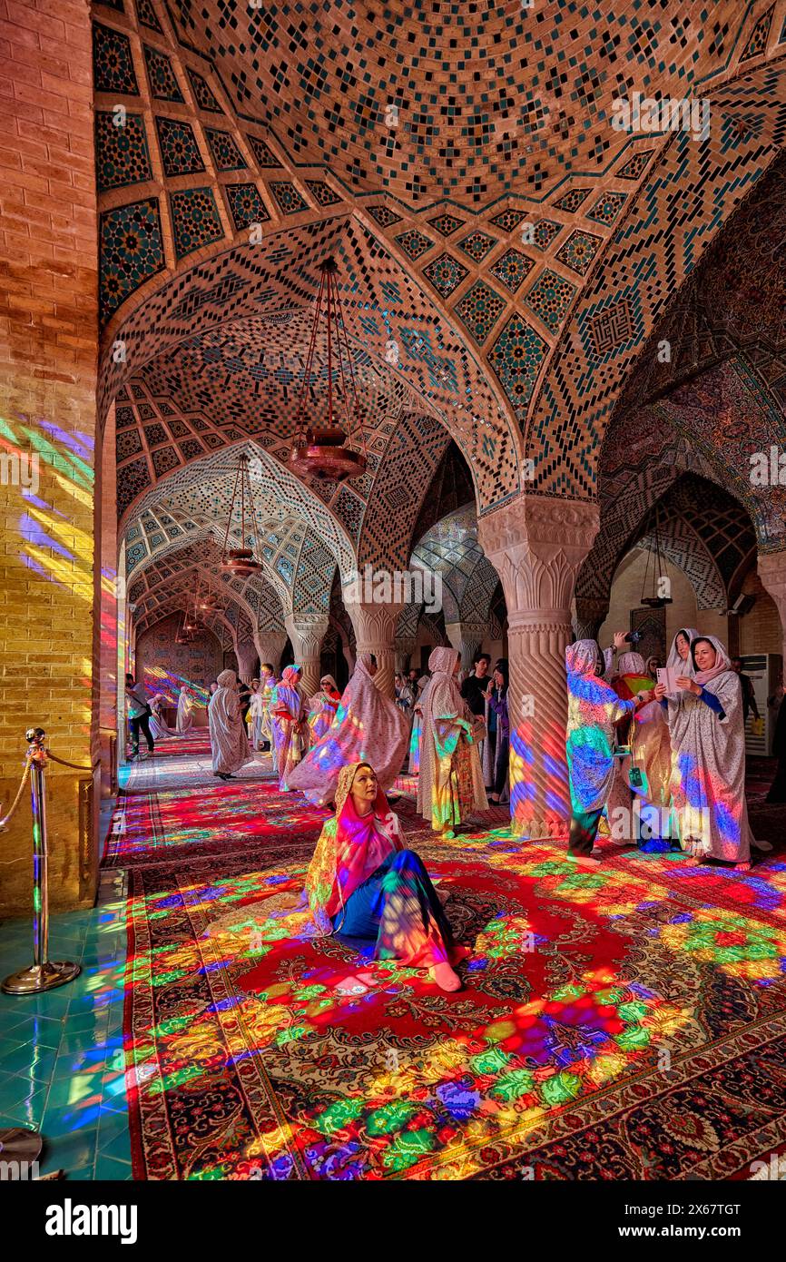 Eine Frau sitzt im Licht von bunten Buntglasfenstern in der Nasir al-Mulk Moschee aus dem 19. Jahrhundert, auch bekannt als die Rosa Moschee. Shiraz, Iran. Stockfoto