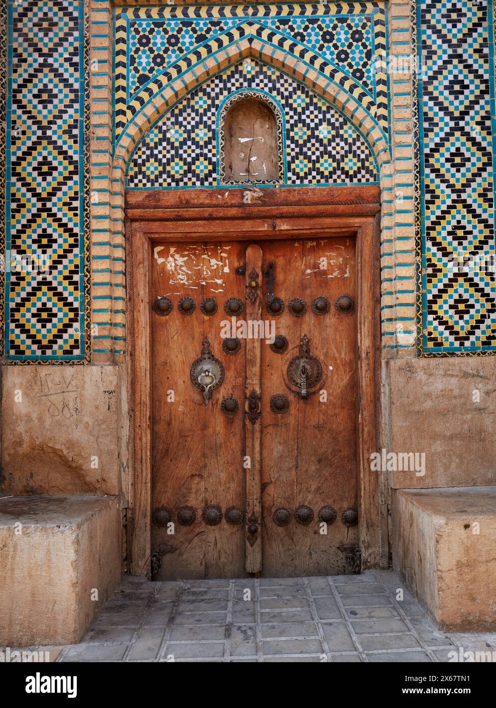 Geschlossene Holztür eines alten Gebäudes mit zwei separaten Klopfern - Metallstange für Männer und Metallring für Frauen. Shiraz, Iran. Stockfoto