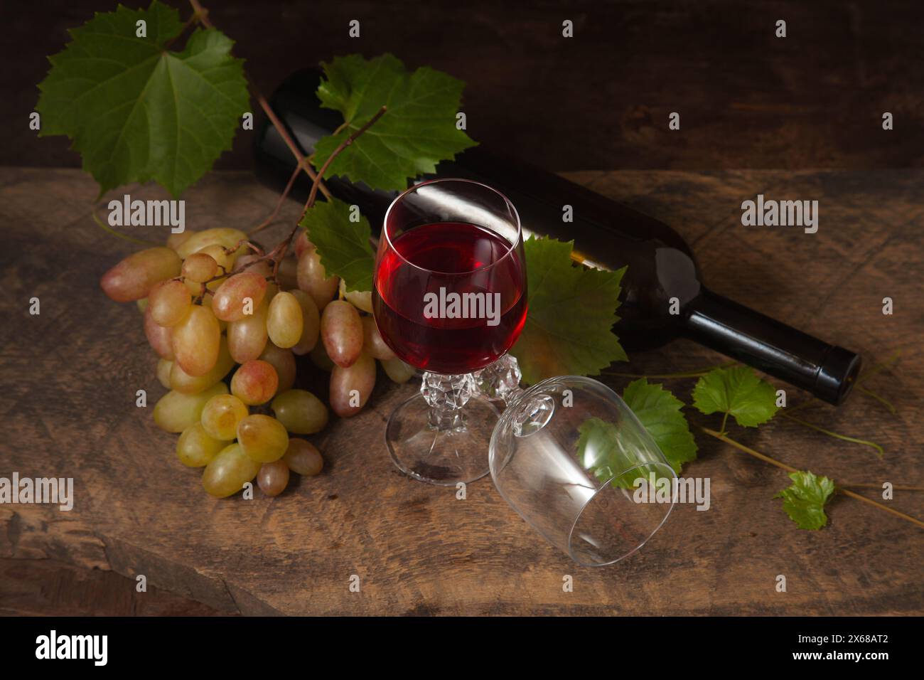 Das Konzept eines köstlichen alkoholischen Getränks, Wein und Trauben. Weinflasche, Trauben, leeres Glas und Glas Rotwein auf dunklem rustikalem holzbalkon Stockfoto