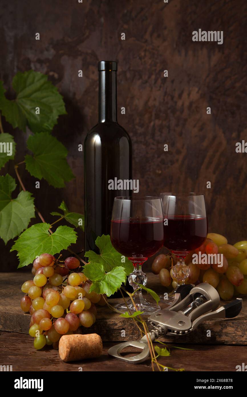Das Konzept eines köstlichen alkoholischen Getränks, Wein und Trauben. Weinflasche, Kork, Korkenzieher, Gläser Rotwein und Trauben auf dunklem rustikalem wo Stockfoto