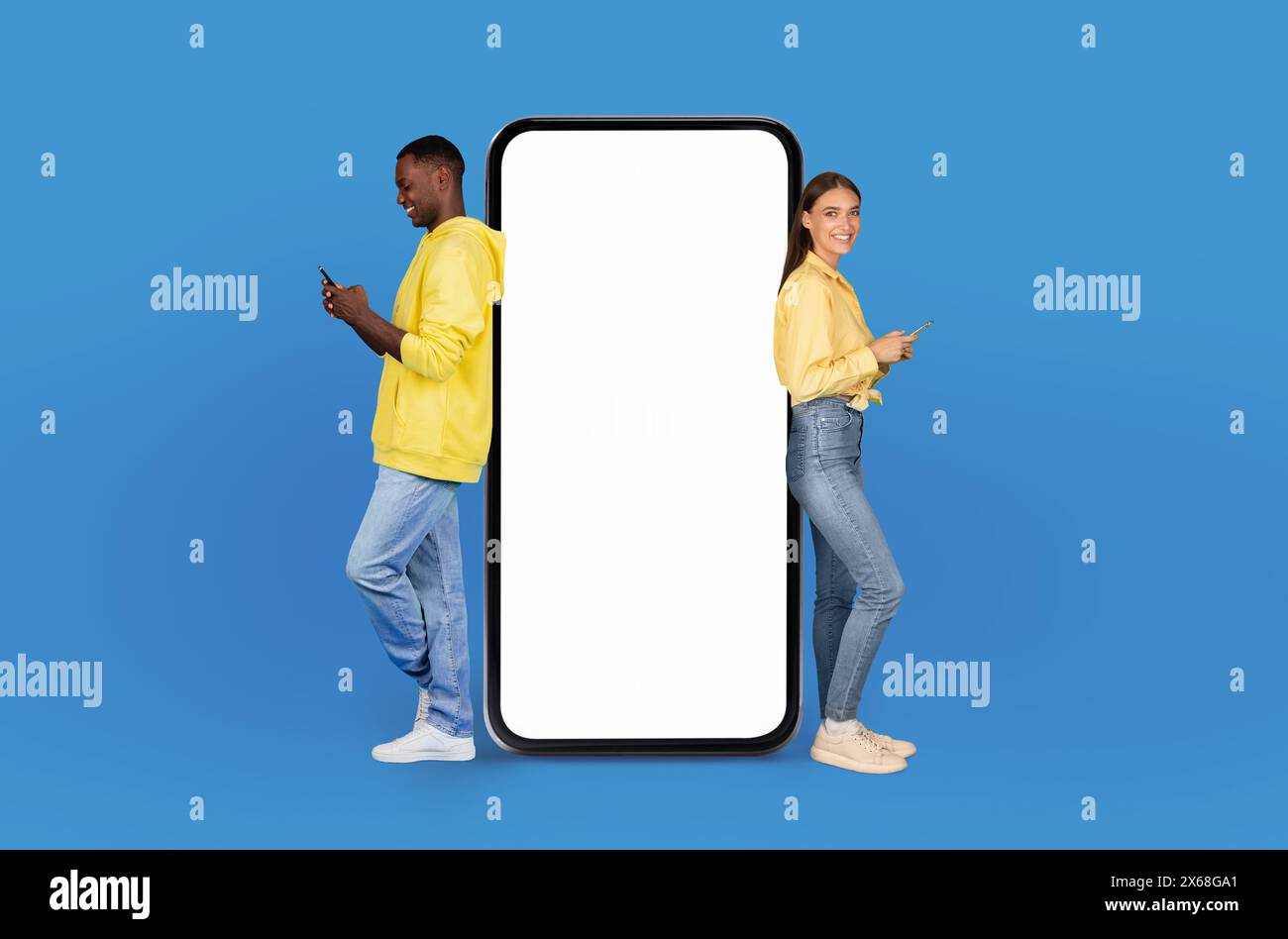 Junge Paare, die ihre Smartphones benutzen, getrennt durch den riesigen leeren Bildschirm Stockfoto