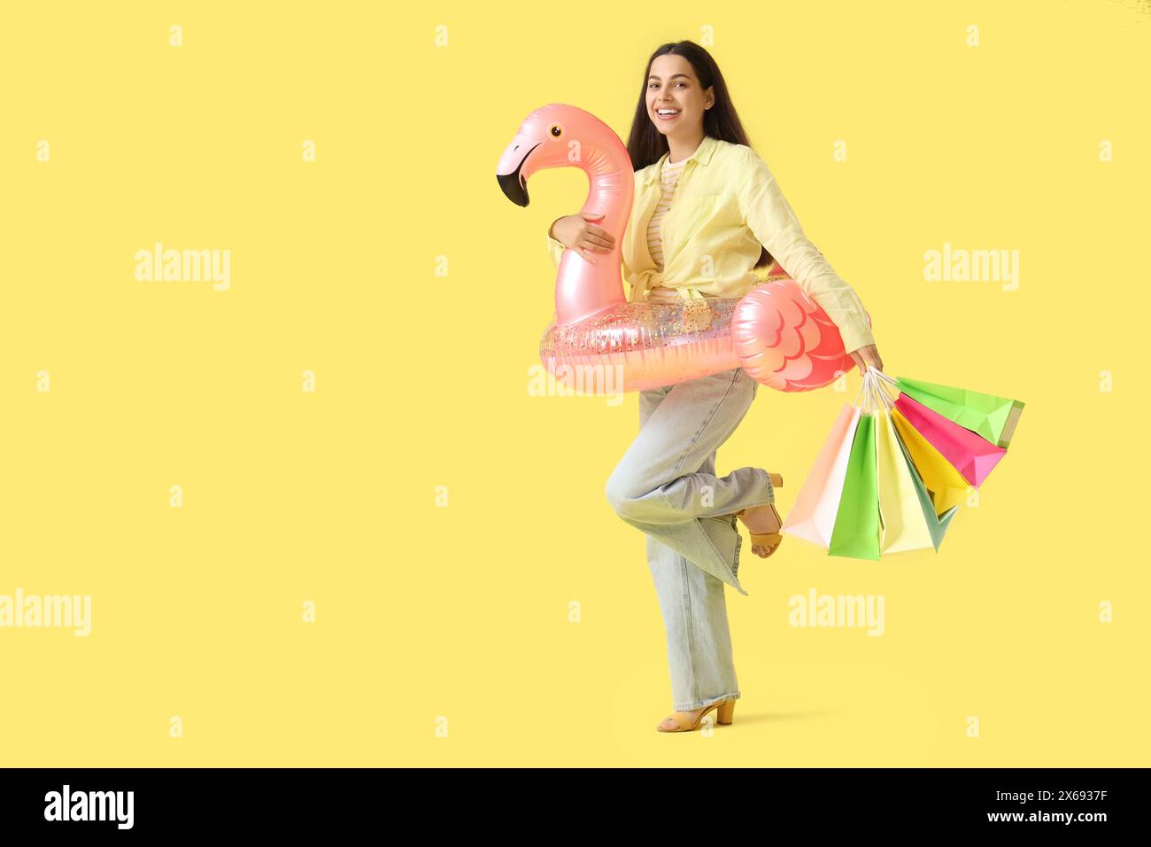 Schöne junge glückliche Frau, die aufblasbaren Ring und Einkaufstaschen auf gelbem Hintergrund hält Stockfoto