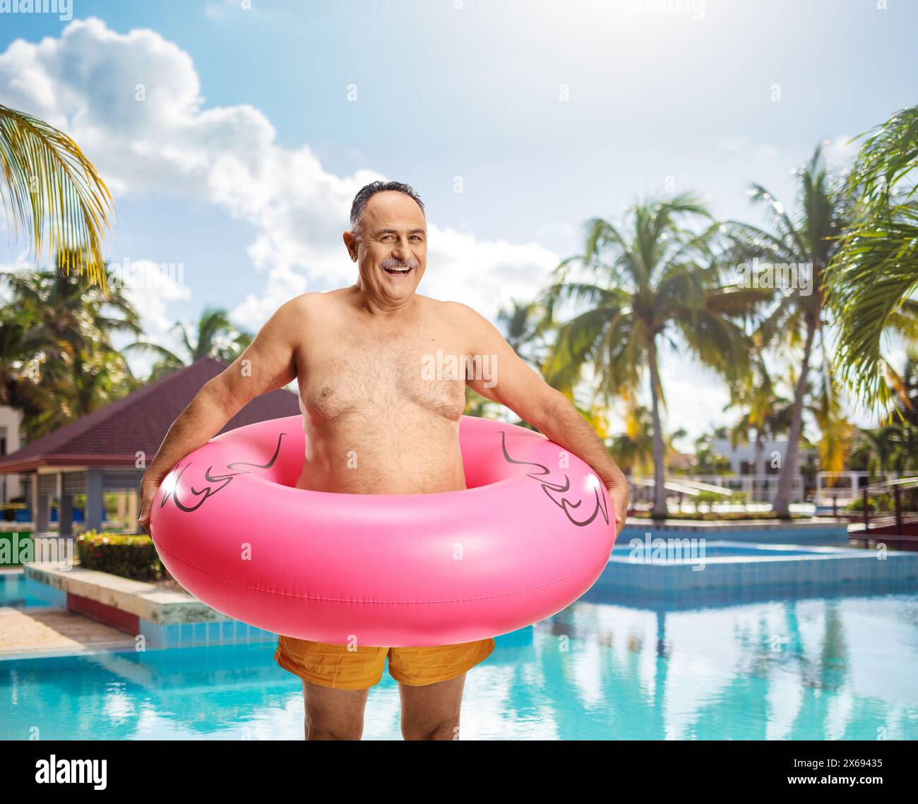 Glücklicher reifer Mann mit Badehosen und aufblasbarem Flamingo-Gummiring am Pool Stockfoto