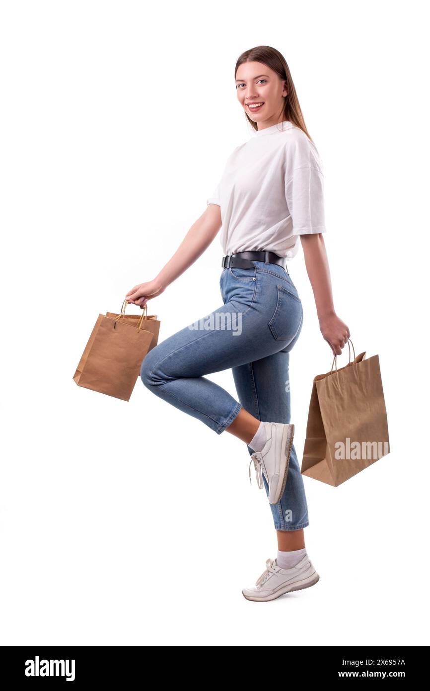 Wunderschönes glückliches lächelndes kaukasisches Mädchen Shopper in weißem T-Shirt und blauer Jeans, das mit Papiereinkaufstaschen auf weißem Hintergrund springt Stockfoto