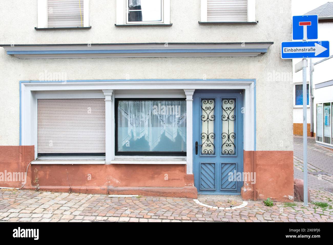 Alte blaue Tür mit Glasfenstern führt zu einem grauen Haus. Straße mit Häusern und singen in Deutschland. Stockfoto