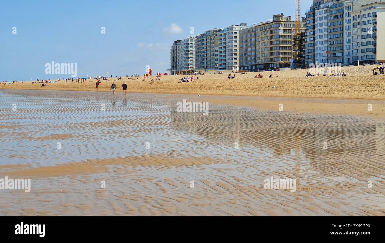 Leute laufen am Sandstrand am Meer mit vielen Häusern und Hotel am Abend. Stockfoto
