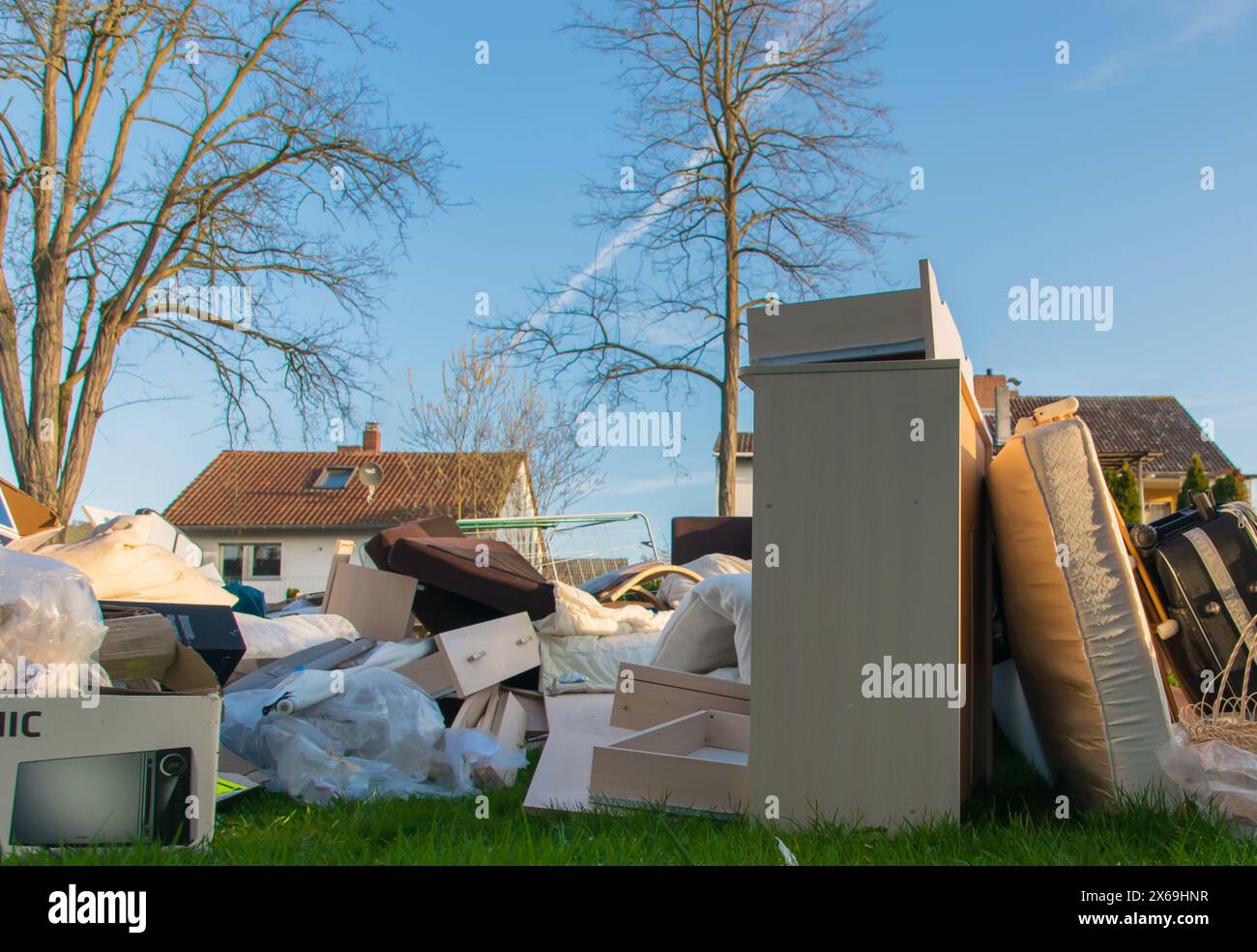 Verschwendung in einer Stadt in der Nähe des hauses. Großer Müll mit alten Holzmöbeln, Spielzeug, Kisten, Plastiktüten auf einer Straße und grünem Gras im Frühling sonnigen Müllkippe Stockfoto