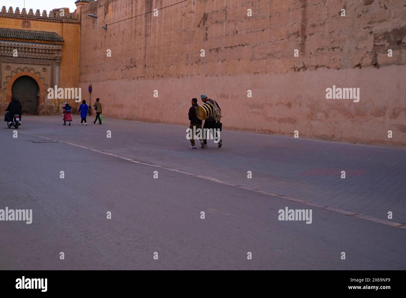 Die Menschen laufen entlang der hohen Mauer Red City Marrakesch, beeilen sich über Geschäfte, authentische afrikanische Stadtlandschaft, tägliche Aktivitäten und Interaktionen, die die Menschen leben Stockfoto