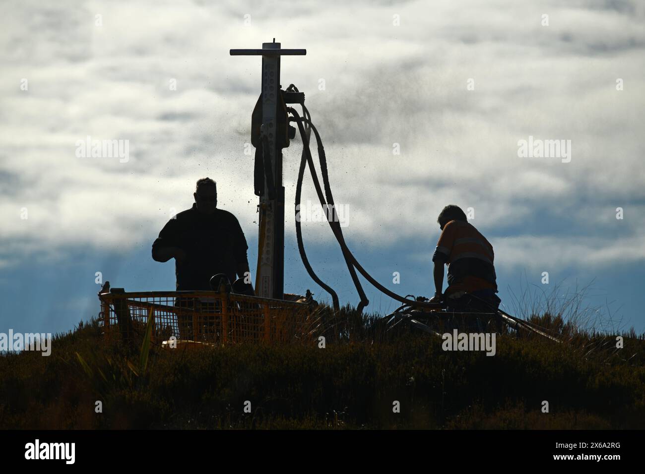 Silhouette von Bohrern, die ein tragbares Bohrgerät betreiben, um ein 10 Meter langes Loch auf dem Gipfel des Mount Morgan mit Blick auf das Haupiri Valley, West Co. Zu senken Stockfoto