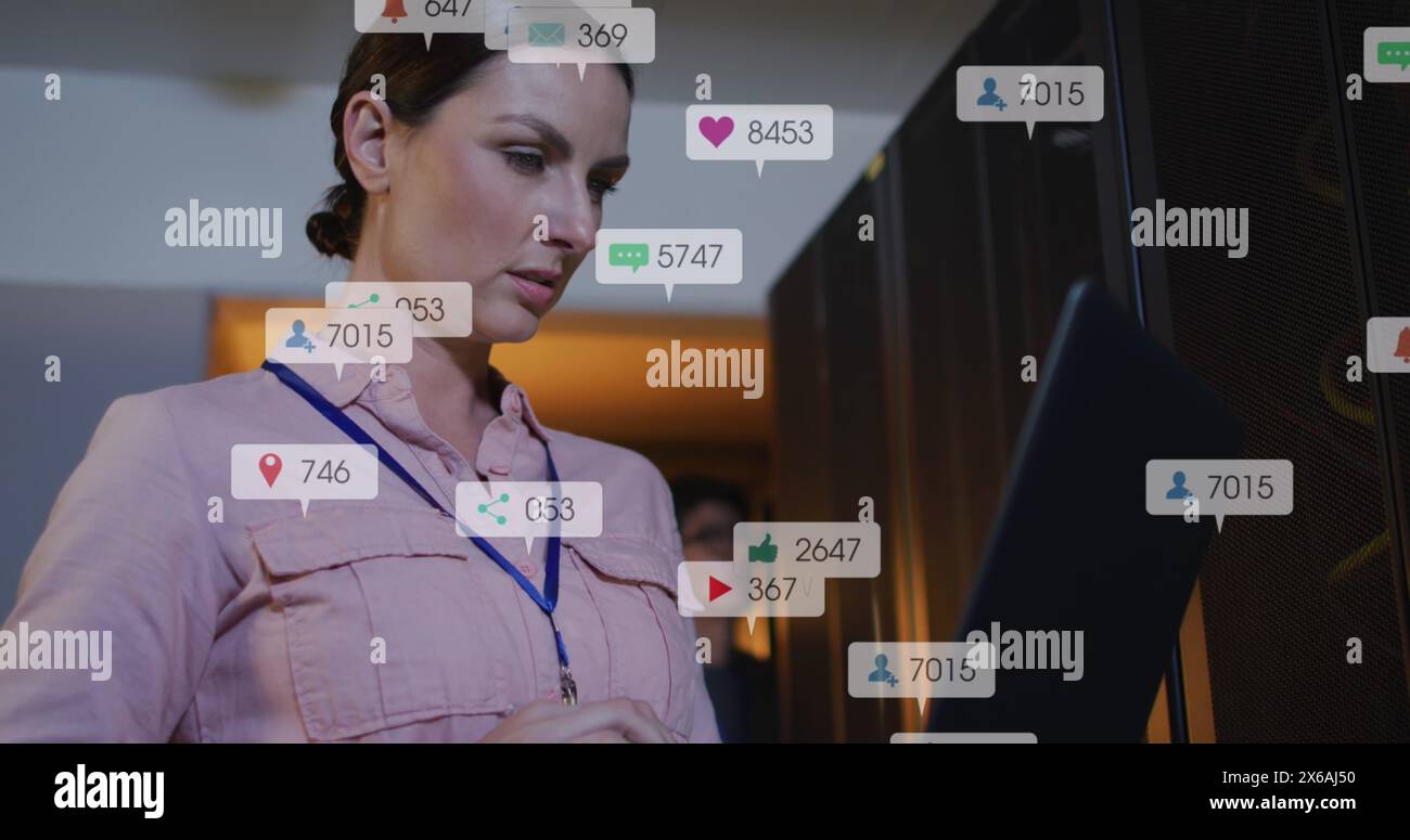 Bild von Social-Media-Ikonen über kaukasischer Ingenieurin, die im Serverraum einen Laptop benutzt Stockfoto