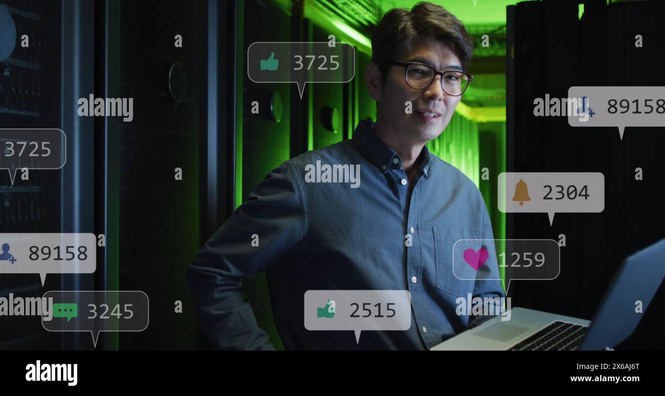 Bild von Social-Media-Ikonen über asiatischen männlichen Ingenieur mit Laptop im Serverraum Stockfoto