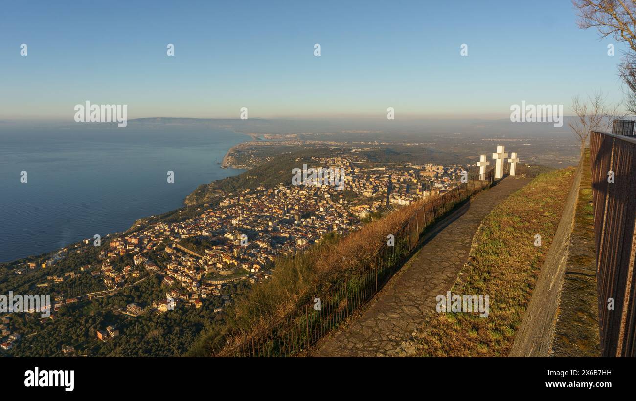Blick über die Stadt an der mittelmeerküste vom Aussichtspunkt Monte Sant'Elia mit drei weißen Kreuzen während der goldenen Stunde, PALMI, Kalabrien, Italien Stockfoto
