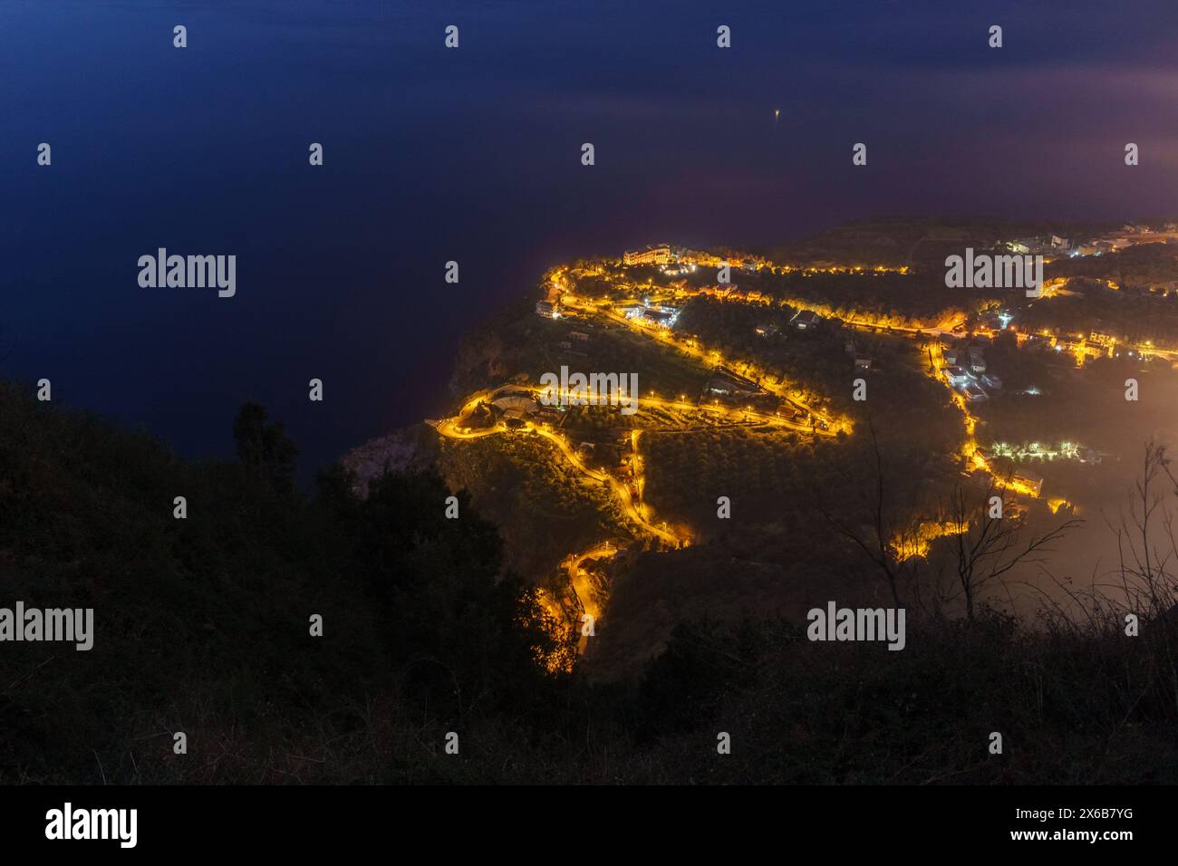 Luftaufnahme auf der beleuchteten Serpentinenküste am mittelmeer aus der Abenddämmerung in der Nacht, PALMI, Kalabrien, Italien Stockfoto