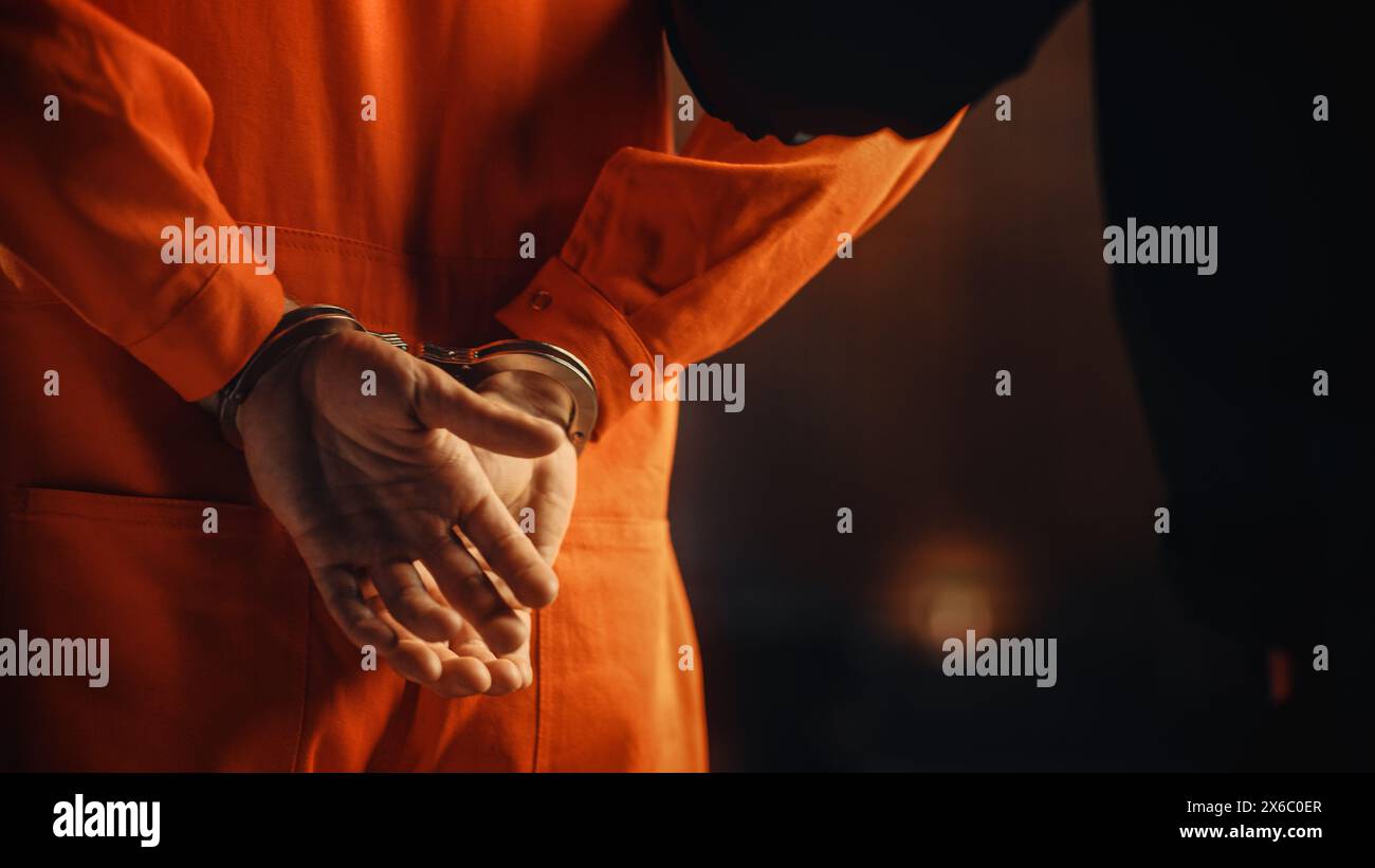 Filmische Nahaufnahmen eines mit Handschellen gefesselten Sträflings bei einem Prozess vor Gericht. Handschellen an den Angeklagten im Jumpsuit in Orange. Strafandrohter verurteilt, Gefängnisstrafe zu verbüßen. Stockfoto