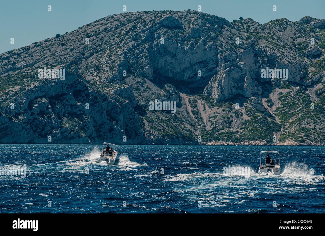 Schnellboote fahren in der Nähe von felsigen Calanques unter klarem Himmel Stockfoto