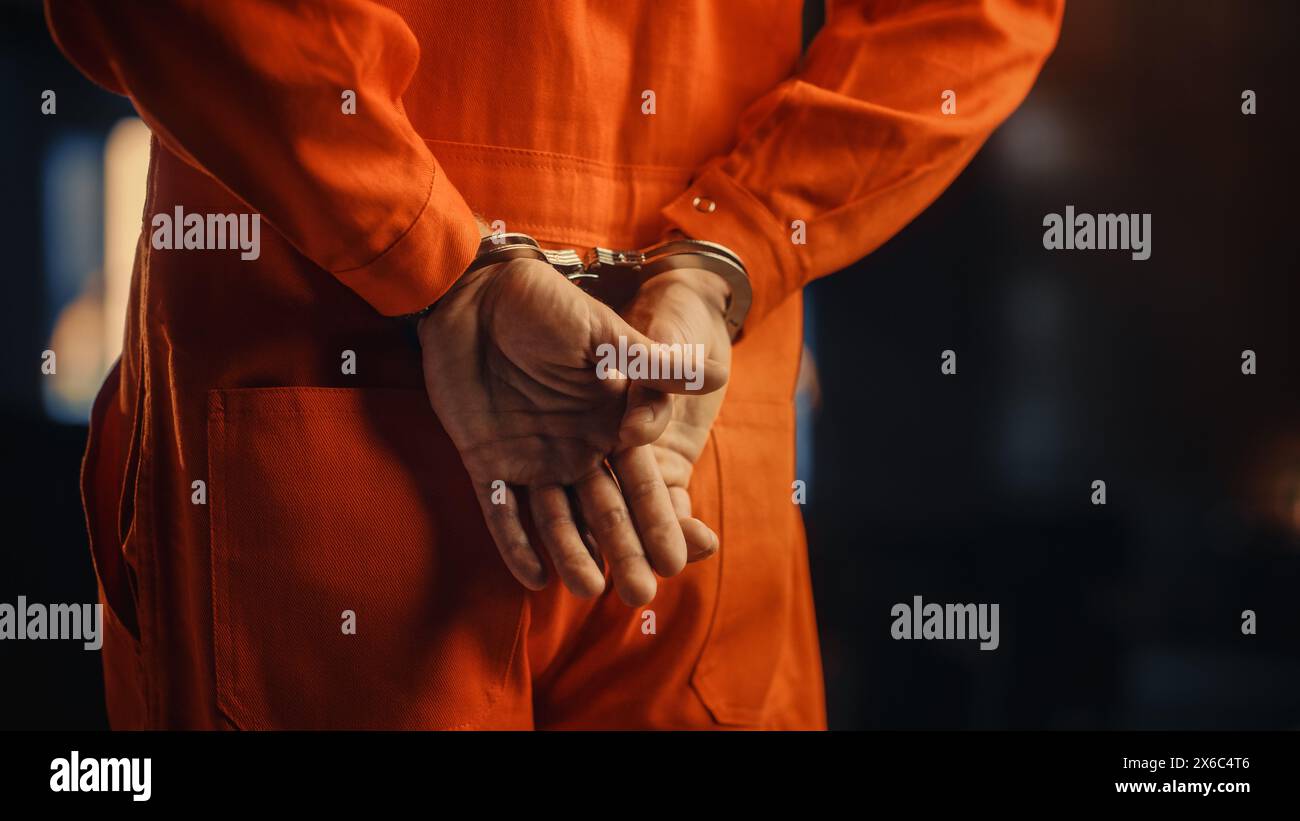 Filmische Nahaufnahmen eines mit Handschellen gefesselten Sträflings bei einem Prozess vor Gericht. Handschellen an den Angeklagten im Jumpsuit in Orange. Strafandrohter verurteilt, Gefängnisstrafe zu verbüßen. Stockfoto
