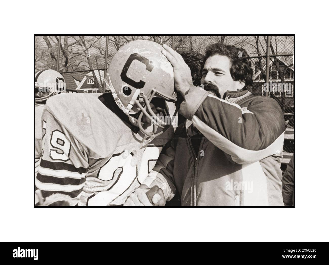 Ein Trainer der Canarsie High School Fußballmannschaft gratuliert einem Spieler nach einem Sieg, indem er die Hand schüttelt und seinen Helm aufklebt. Im Midwood Field in Brooklyn 1982. Stockfoto