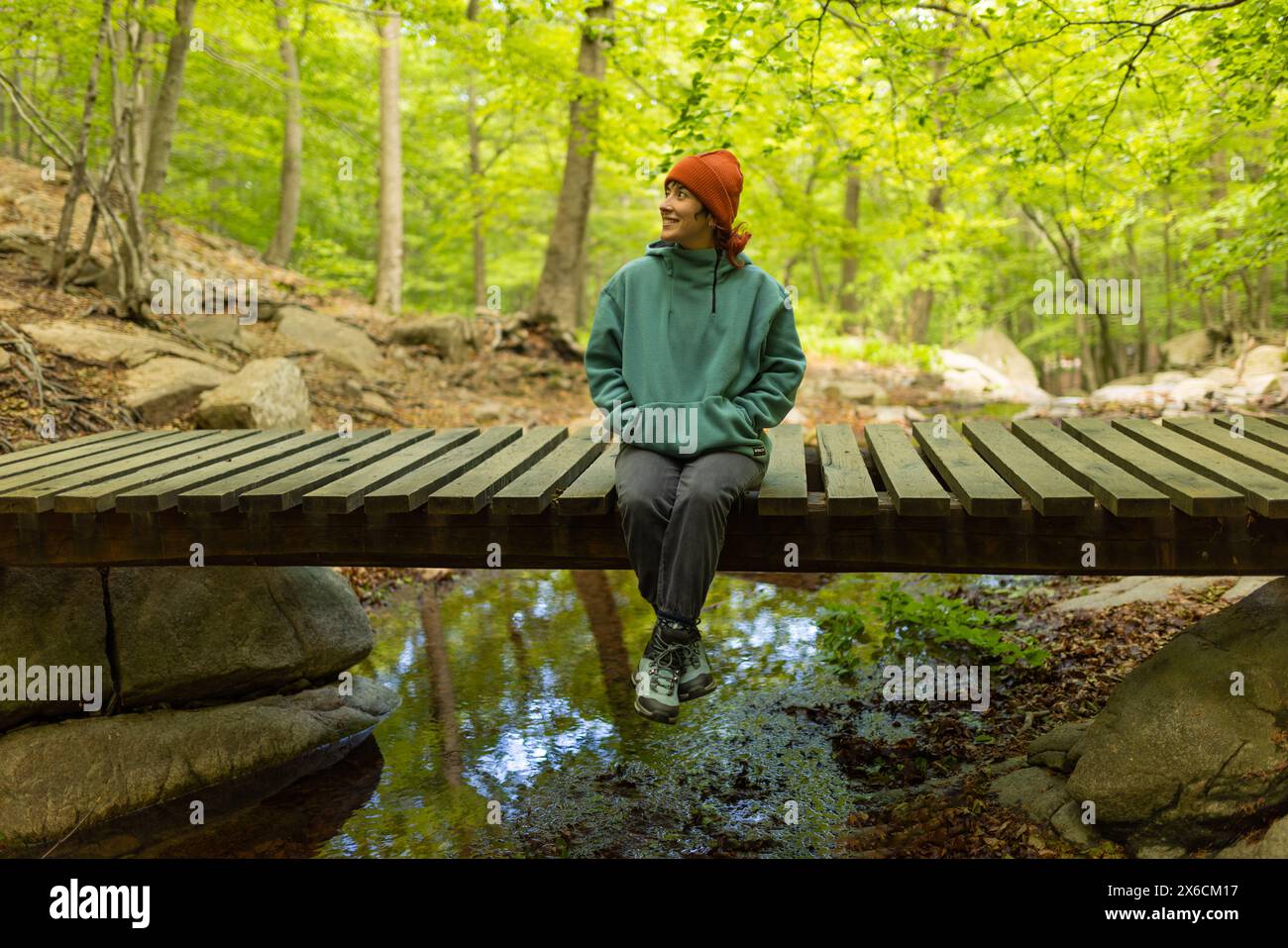 Frau im Wald sitzt auf einer Brücke mit orangefarbenem Hut, auf einer Reise auf der Suche nach neuen Entdeckungen Stockfoto