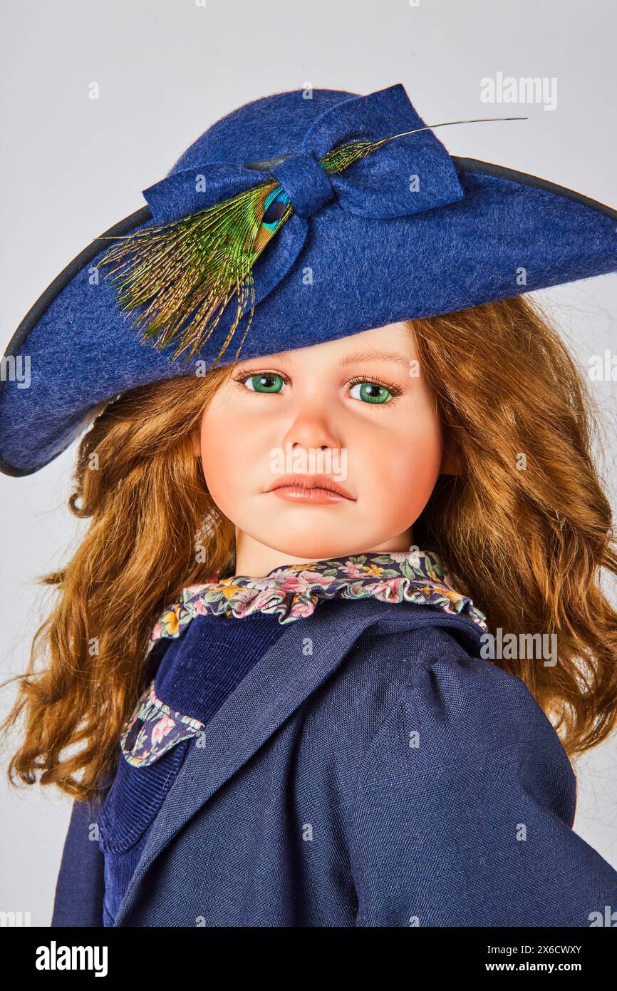 Elegante Mädchenpuppe in blauem Hut und Mantel mit Pfauenfeder, Studio-Porträt Stockfoto