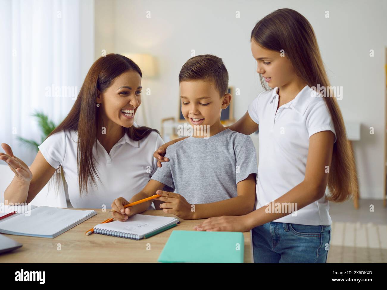 Glückliche, fürsorgliche Mutter, die Hausaufgaben mit ihrem Sohn und ihrer Tochter macht Stockfoto