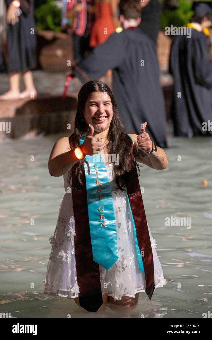 Austin Texas USA, 11. Mai 2014: Eine College-Absolvent der ersten Generation an der University of Texas at Austin, die noch einige ihrer Abschlussjubiläen trägt, zeigt sich ihrer stolzen Familie gegenüber, während sie unmittelbar nach der Frühjahrsfeier im Littlefield Fountain waten. Der feierliche Dunk ist eine langjährige Campus-Tradition. ©Bob Daemmrich Stockfoto