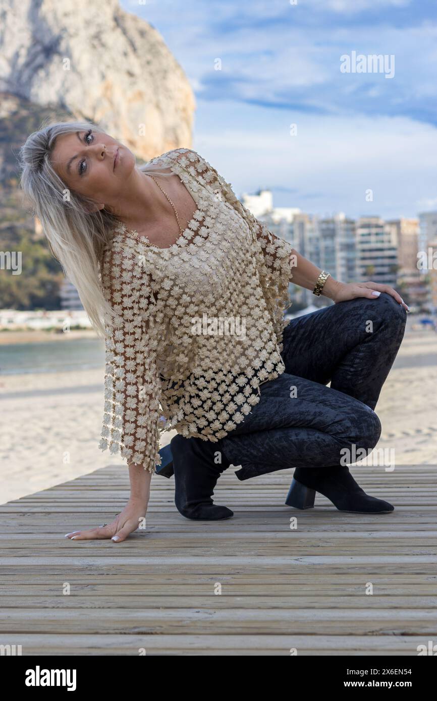 Dieses Bild fängt die ruhige Schönheit einer Frau am Strand während der goldenen Stunde ein. Ihre anmutige Pose vor der ruhigen Kulisse des Ozeans und Stockfoto