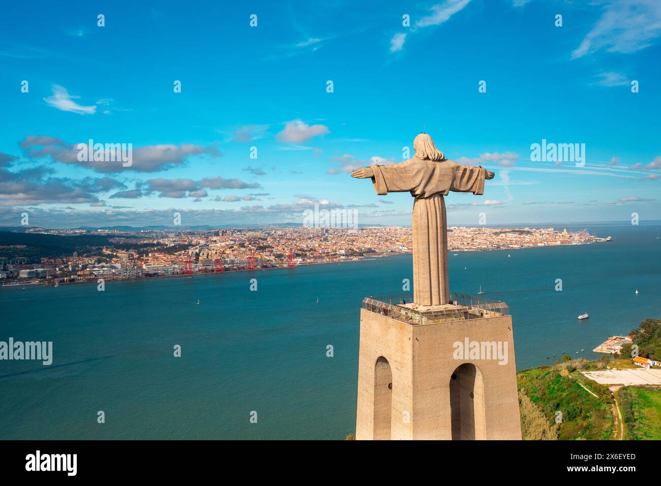Blick aus der Vogelperspektive auf die Christusstatue mit Blick auf den Fluss Tejo und die Stadtlandschaft unter blauem Himmel. Katholisches Denkmal und Stadt aus der Vogelperspektive. Lissabon, Portugal Stockfoto