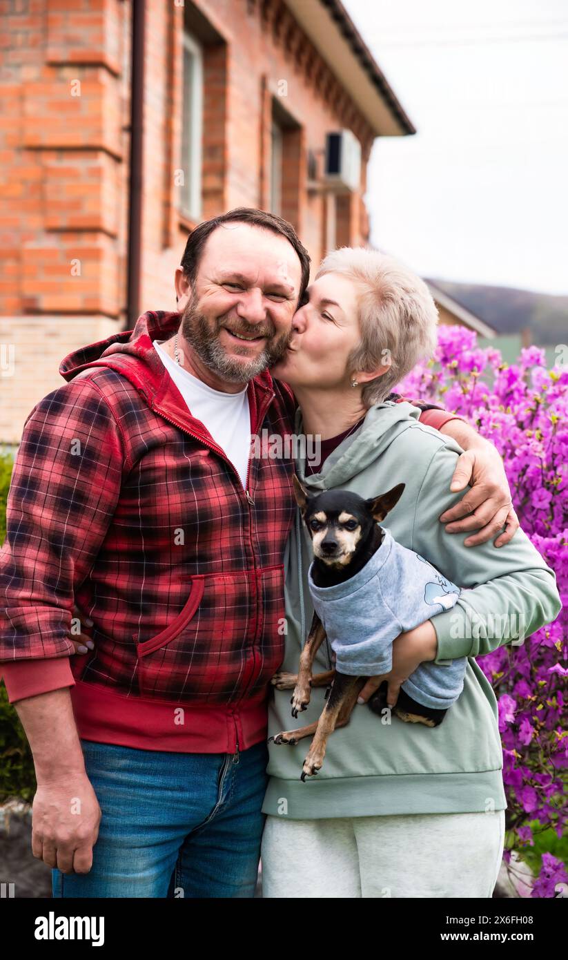 Reifes russisches Ehepaar ksst und umarmt sich in der Nhe des  Bltenstrauchs aus Rhododendron, hlt einen Hund Stockfotografie - Alamy