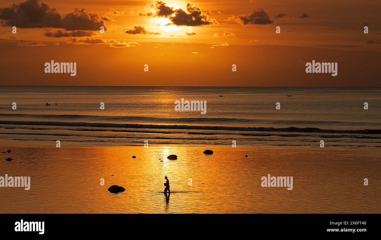 Sonnenuntergang auf der Suche nach Nahrungssuche, atemberaubender Sonnenuntergang über Bining Beach, Bali, die ruhige Schönheit der Wellen, die sanft gegen die Riffe krachen, während die Menschen spazieren gehen Stockfoto