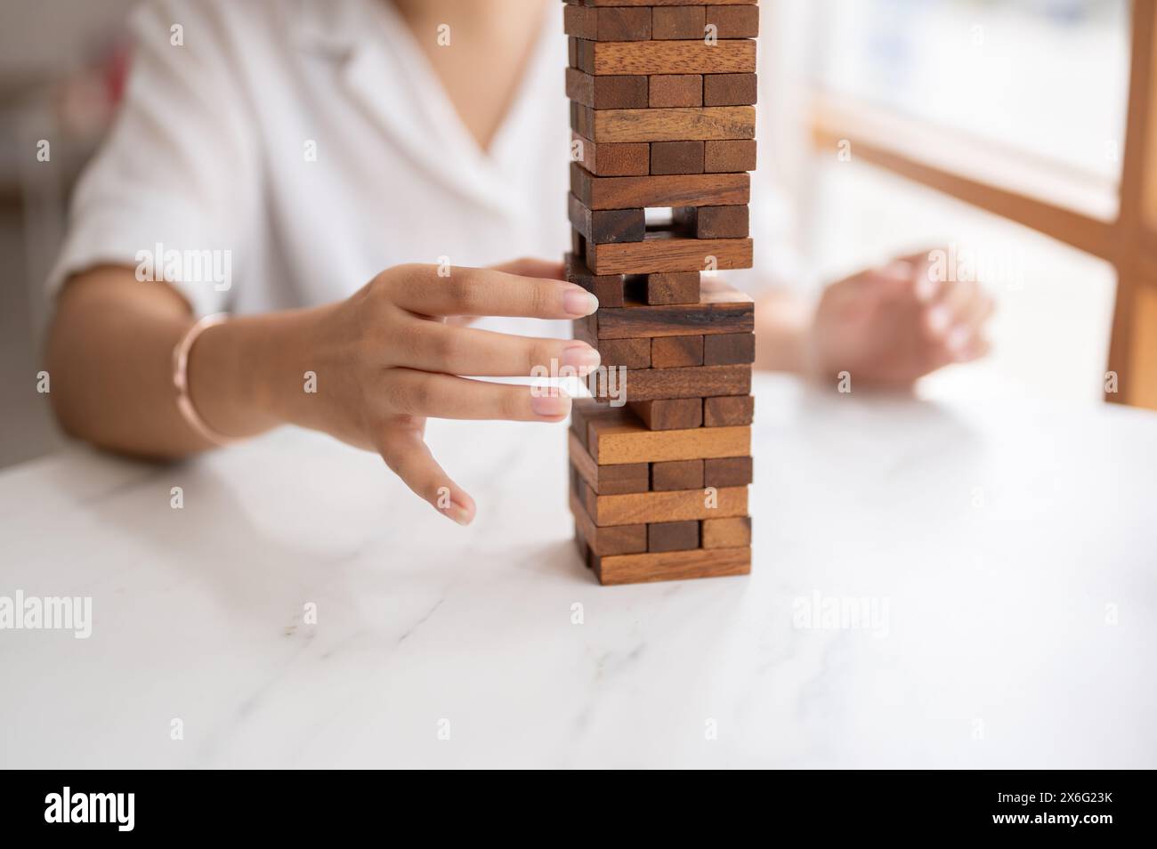 Eine Nahaufnahme einer Frau achtet darauf, ein Holzblockspiel an einem Tisch zu spielen und einen Holzblock zu bewegen. Spielzeug, Spiel, Freizeit Stockfoto