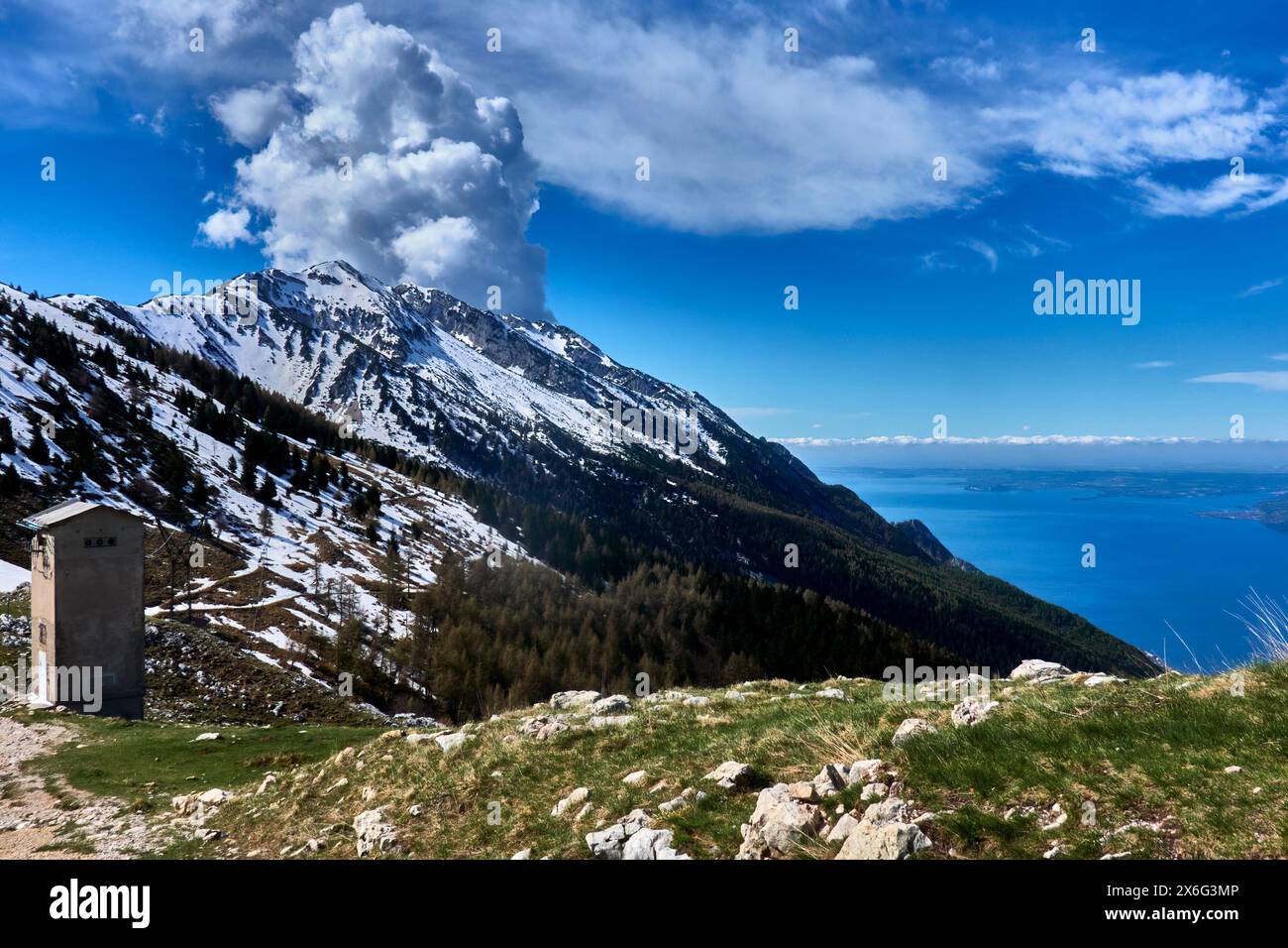 Aufsteigende Wolken hinter den schneebedeckten Gipfeln des Monte Baldo mit dem Gardasee im Hintergrund Stockfoto