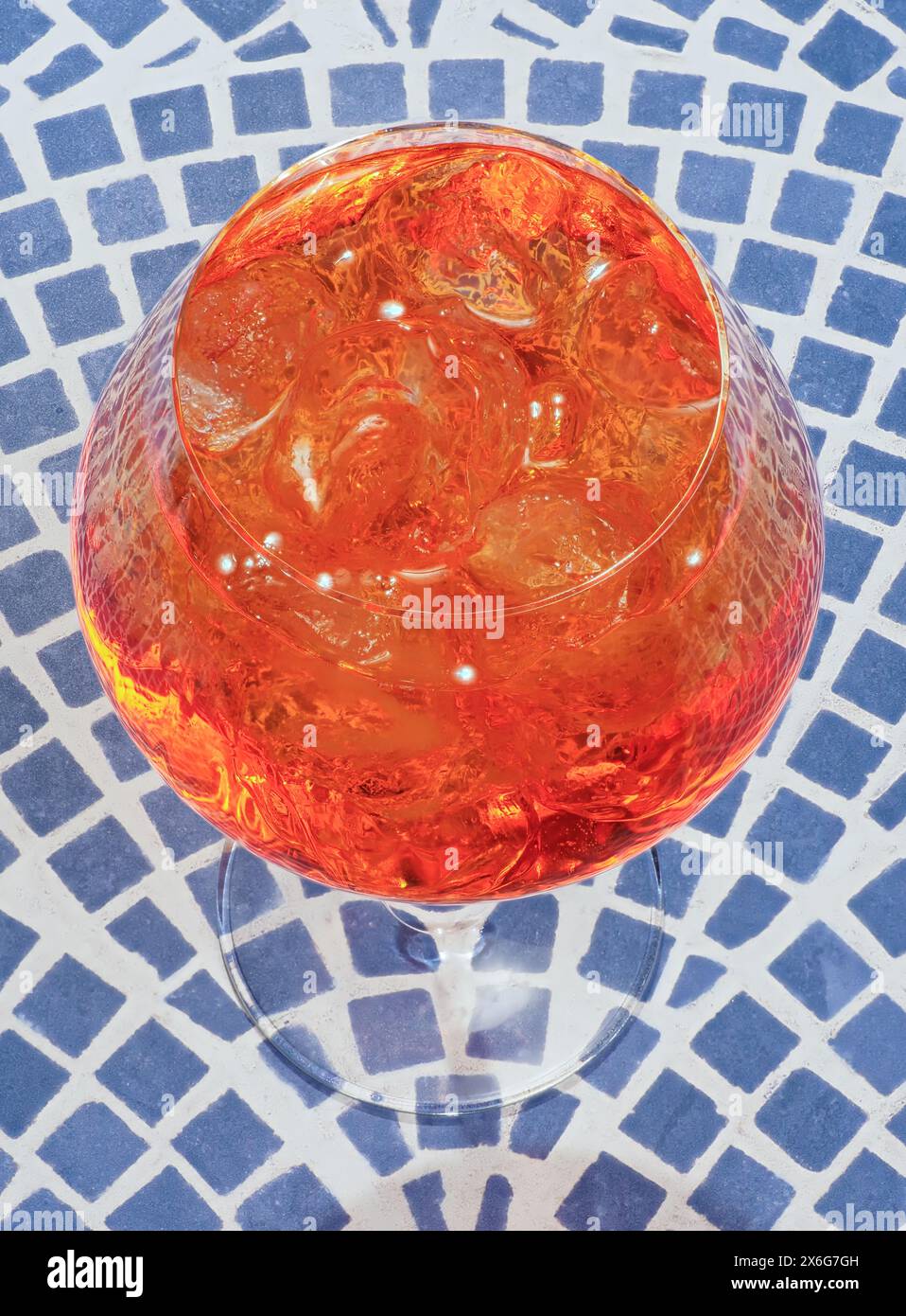 Nahaufnahme eines Aperol Spritz Cocktails mit Eiswürfeln, im Sonnenlicht glühend, auf einer gemusterten Oberfläche Stockfoto