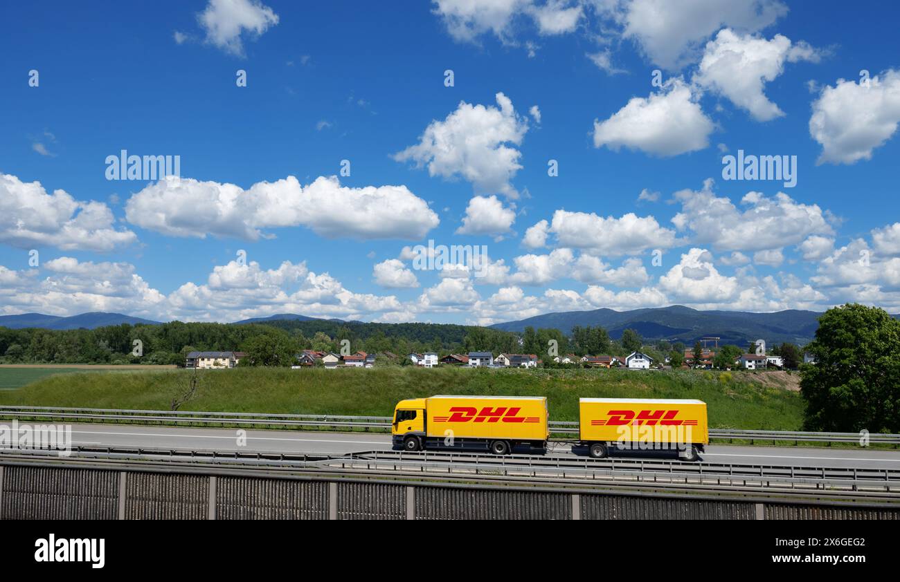 Ein gelber Lkw mit DHL-Logo fährt auf einer Autobahn bei Deggendorf mit Bayerischem Wald im Hintergrund, Niederbayern Stockfoto