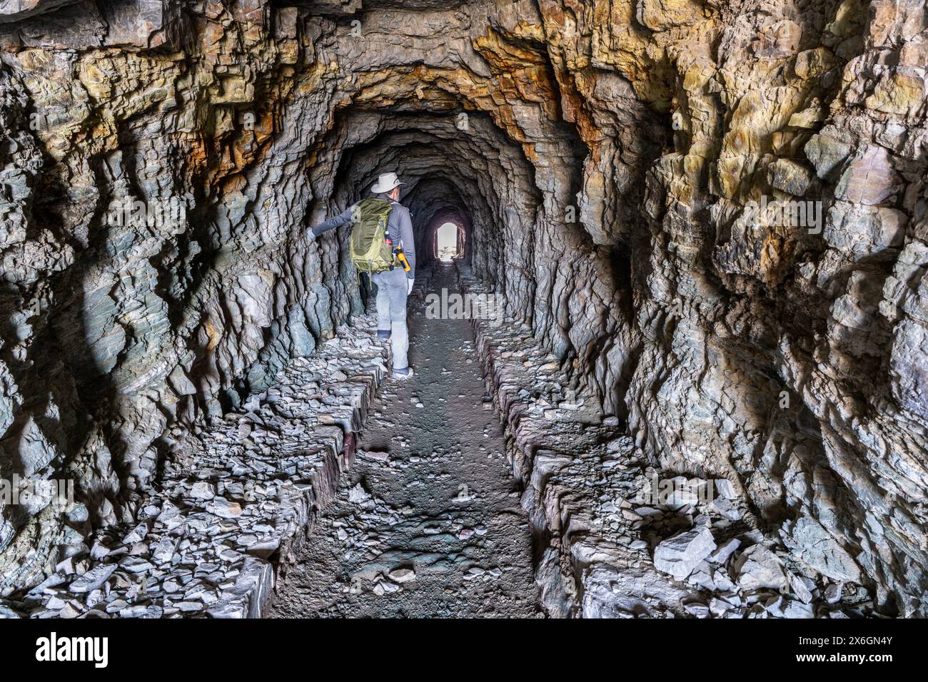 Reife Caucasian man Wanderer steht in einem Fußgängertunnel, der durch Red Argillith und Quarzitgestein gesprengt wurde, Ptarmigan Tunnel, Glacier National Park, Stockfoto