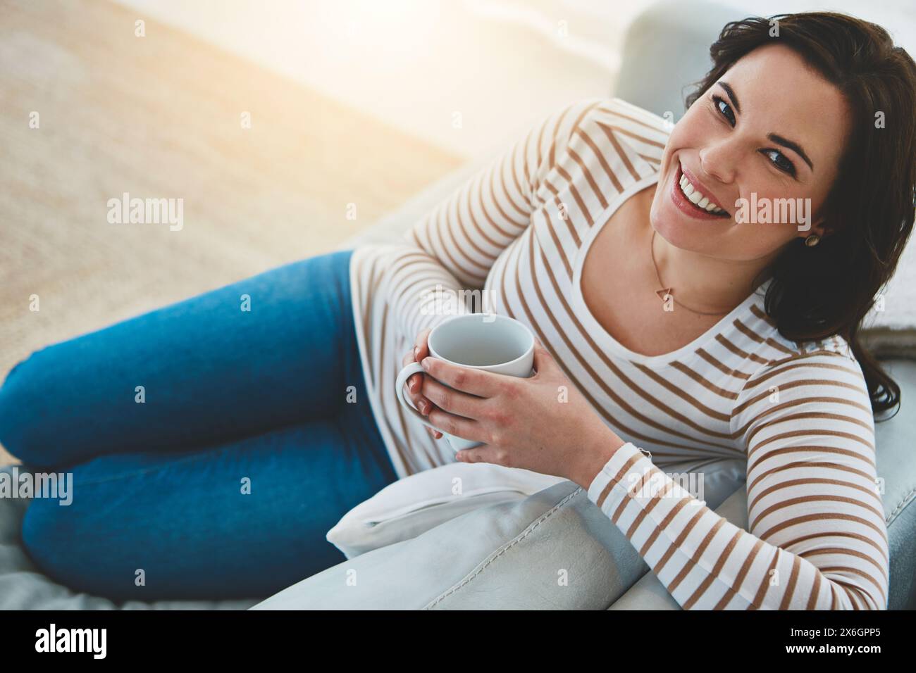 Frau, Kaffee und Happy for Porträt auf Sofa zum Entspannen in der Pause, zu Hause und Espresso im Wohnzimmer. Person, Teetasse und Lächeln auf der Couch in der Lounge mit Stockfoto