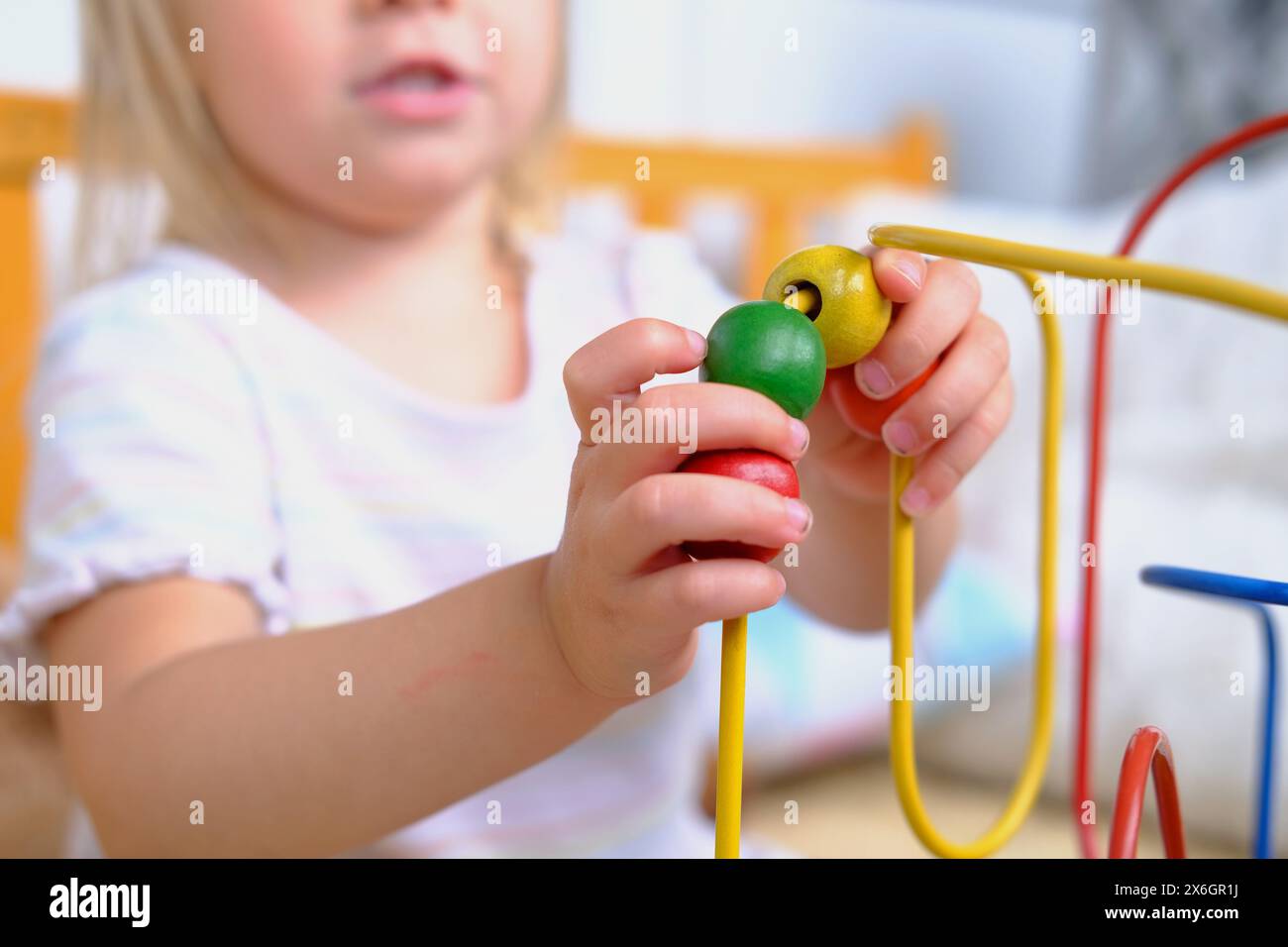 Mädchen 3 Jahre alt spielt mit farbigem hölzernen pädagogischen Labyrinth für Kinder, Nahaufnahme der Hände des süßen Kindes, Entwicklung der Feinmotorik, Konzept Stockfoto