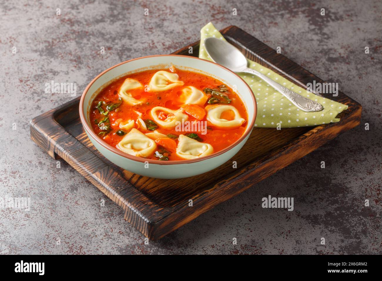 Köstliche cremige Tomaten-Tortellini-Suppe mit Spinat und Gemüse auf dem Teller auf dem Tisch. Horizontal Stockfoto