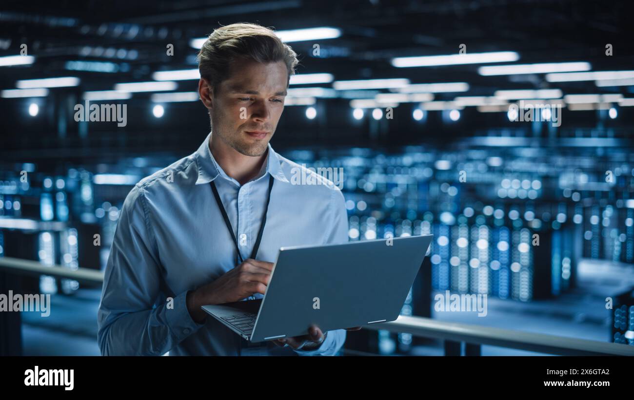 Hübscher, lächelnder IT-Spezialist mit Laptop im Rechenzentrum. Erfolgreicher Geschäftsmann und E-Business-Unternehmer mit Blick auf die Server Farm Cloud Computing Facility. Stockfoto
