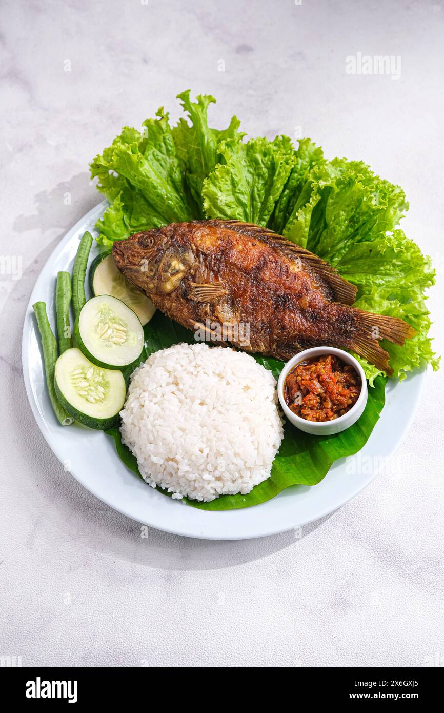 Frittierte Tilapia oder Ikan Nila Goreng serviert mit Salat, Gurke und Sambal auf Teller Stockfoto