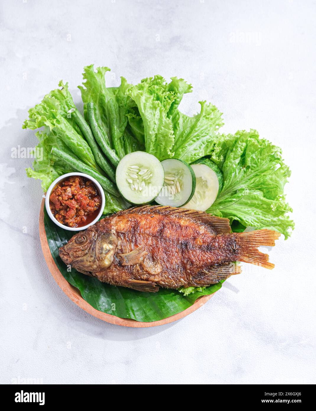 Frittierte Tilapia oder Ikan Nila Goreng serviert mit Salat, Gurke und Sambal auf Teller Stockfoto